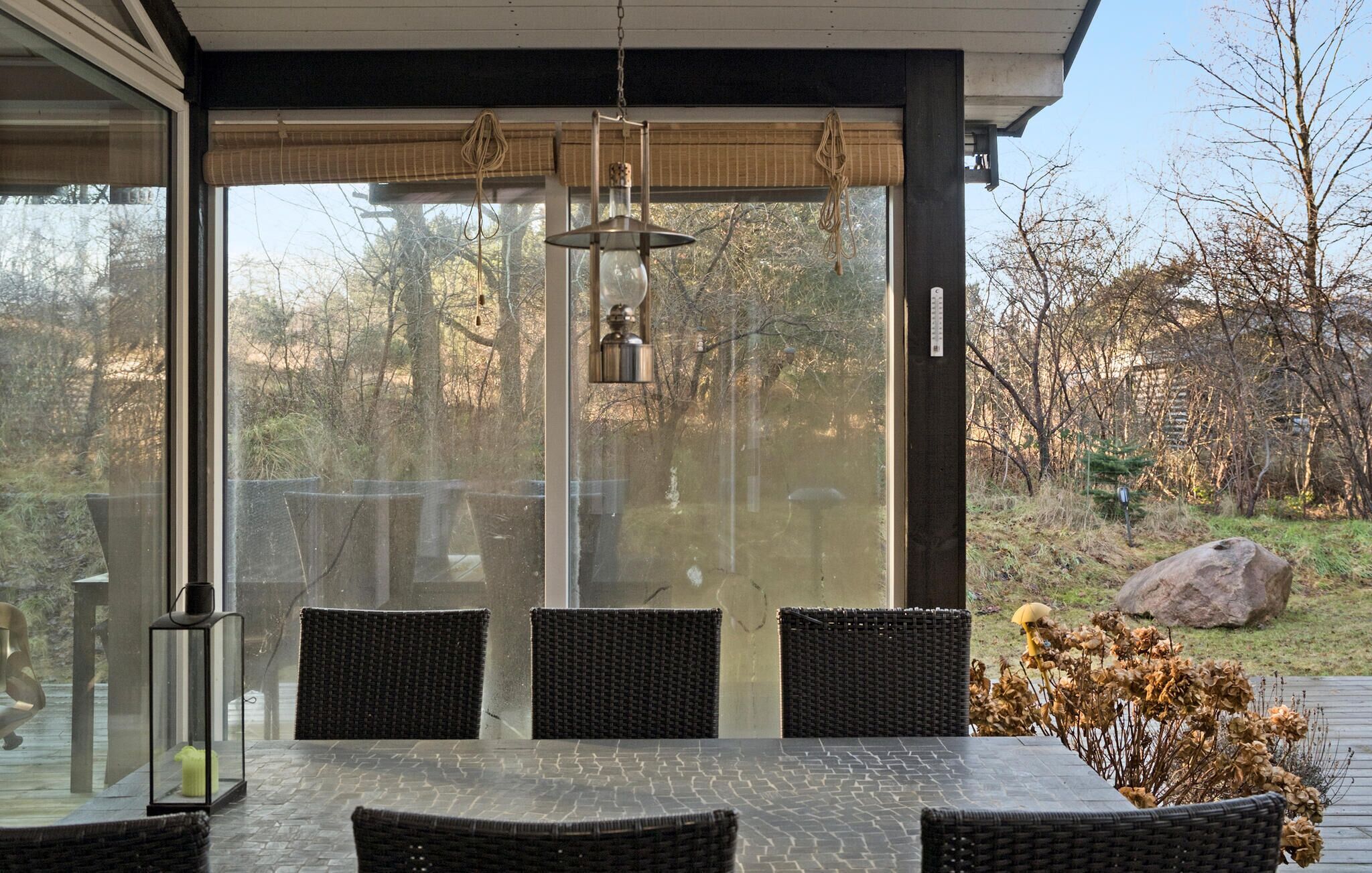 Une terrasse couverte avec une table et des chaises, de grandes fenêtres et un luminaire suspendu.