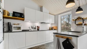 A modern kitchen with white cabinetry, a built-in microwave, a coffee machine, and a window providing a view of trees. - 5 bedroom nice home in Fårevejle (Fårevejle)