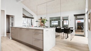 Een moderne keuken met een groot eiland, houten kastjes en een eethoek met zwarte stoelen.