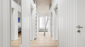 Een gang met witte deuren, een zichtbaar bed en een blauw bord aan de linker muur.
