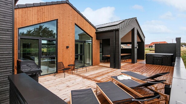 Een modern terras buiten met houten vloer, zwarte lounge fauteuils en een barbecuehoek.