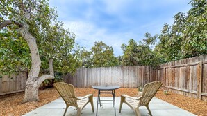 A patio with a table and two chairs, surrounded by a wooden fence and trees. - Peace and Privacy at Bungalow among Avocado Trees (Camarillo)