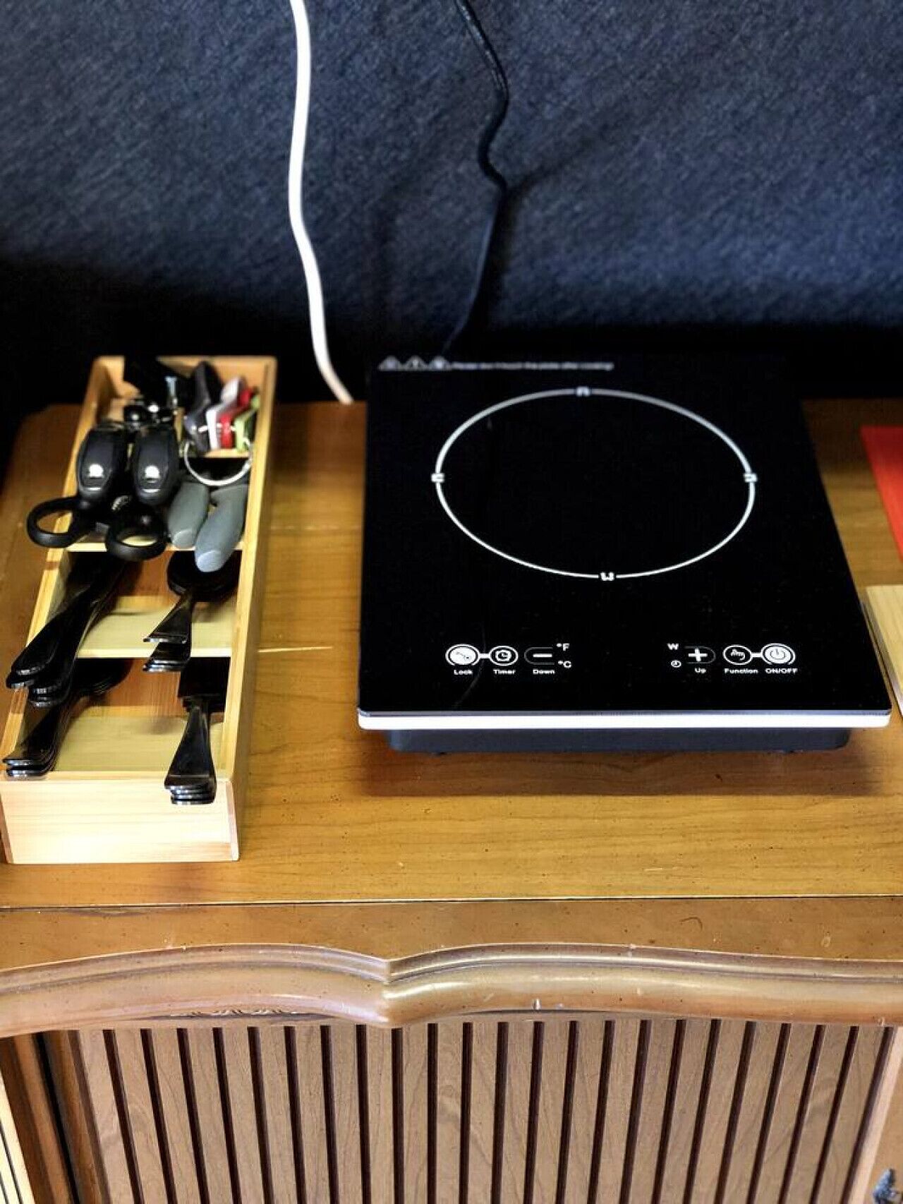 A black induction cooktop with a wooden tray holding various kitchen utensils.