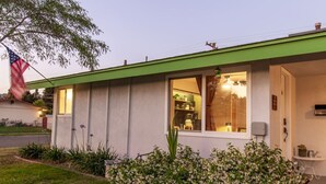 A single-story house with a green roof, a front porch, and a well-maintained garden with flowering plants.