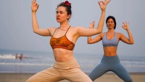 Dos personas realizando una postura de yoga sobre una esterilla en la playa.