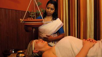 A person lying down with a woman standing beside them, holding a tray with a plant.