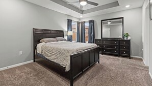 A bedroom with a bed, dark wooden dresser, a ceiling fan, and a large mirror. - Stylish MidModern New Build w/ Extra Apartment (Grandview)