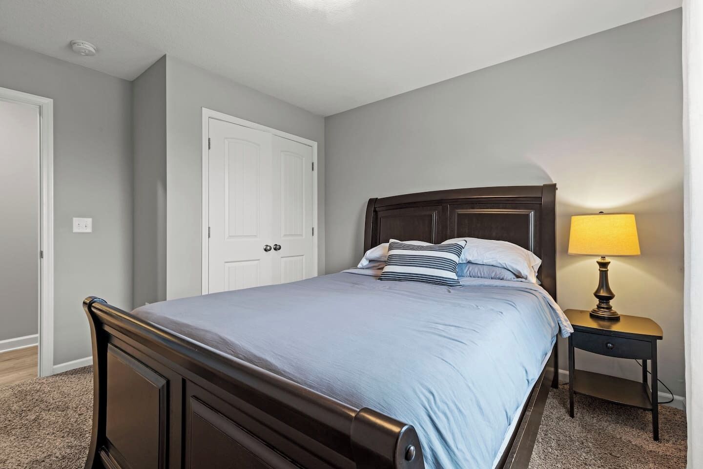 Un dormitorio con cama, una mesita de noche con lámpara y una puerta blanca.