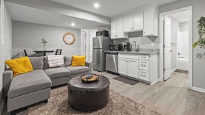 A modern living room with a grey sofa, a round coffee table, and a kitchen area with white cabinets and stainless steel appliances. - Stylish MidModern New Build w/ Extra Apartment (Grandview)