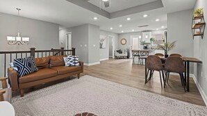 A spacious living area with a brown leather sofa, a dining table with chairs, a ceiling fan, recessed lighting, and a kitchen in the background. - Stylish MidModern New Build w/ Extra Apartment (Grandview)