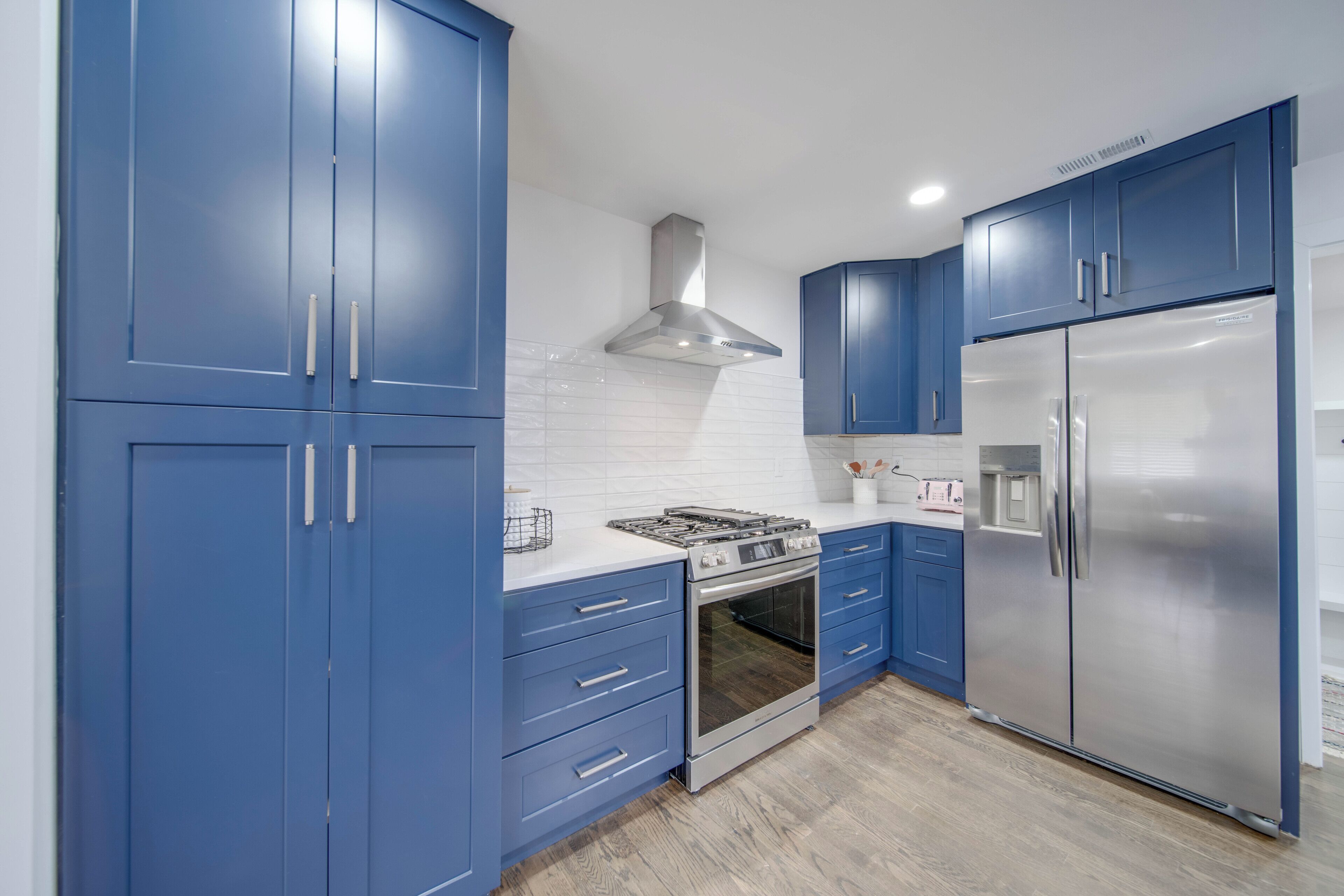 Una cucina moderna con mobili blu, elettrodomestici in acciaio inossidabile e uno schienale in piastrelle bianche.