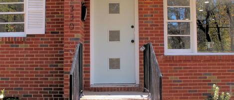 A small brick house with a white door, a small porch, and a window.