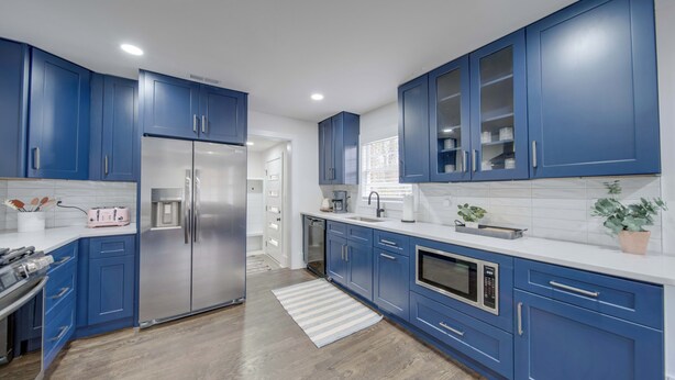 Een moderne keuken met blauwe kastjes, roestvrijstalen apparatuur en een wit aanrecht.