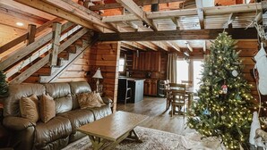 A log cabin interior with a wooden staircase, a leather sofa, a dining table, and a Christmas tree. - Luxury Log Retreat with Hot Tub, Near Homestead & Winery (Paris)