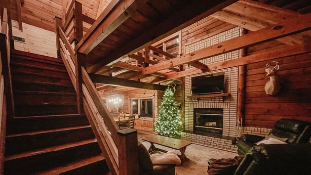 A cozy cabin interior with a wooden staircase, a fireplace, a Christmas tree, and a leather sofa. - Luxury Log Retreat with Hot Tub, Near Homestead & Winery (Paris)