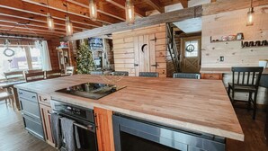 A kitchen with wooden beams, a large island with a built-in stove, and pendant lighting. - Luxury Log Retreat with Hot Tub, Near Homestead & Winery (Paris)
