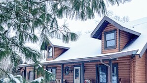 A log cabin with a porch, large windows, and a snow-covered roof. - Luxury Log Retreat with Hot Tub, Near Homestead & Winery (Paris)