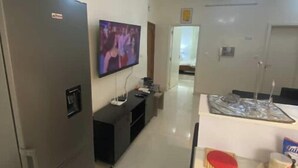 Een compacte keuken met een koelkast, een aan de muur bevestigde televisie, een eettafeltje en een magnetron.