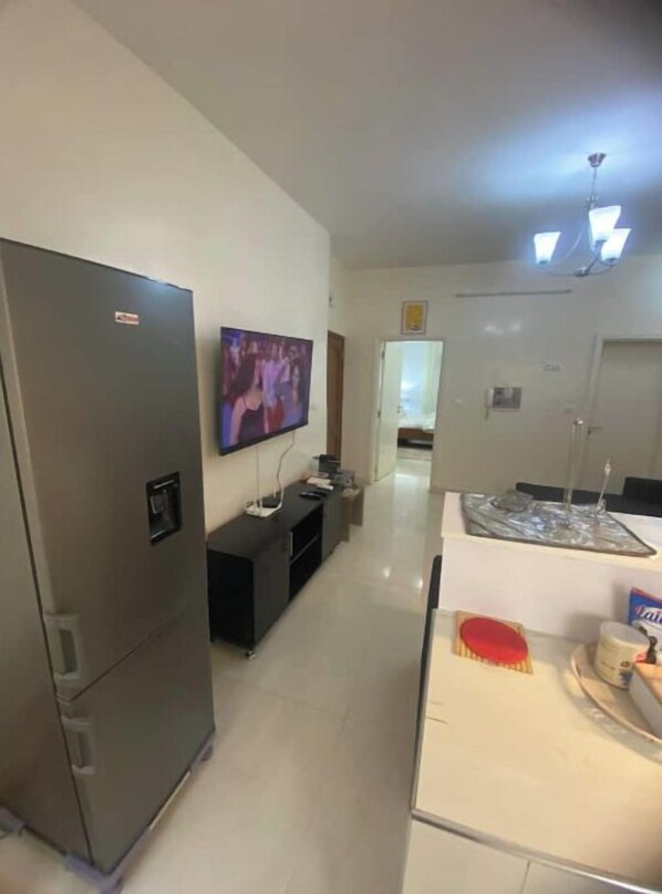 A compact kitchen with a refrigerator, a TV mounted on the wall, a small dining table, and a microwave. - Good plan in Dakar, just perfect (Dakar)