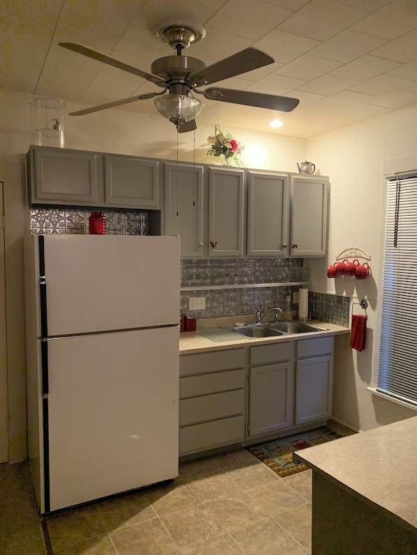 Una cocina con refrigerador, pileta doble y ventilador de techo.