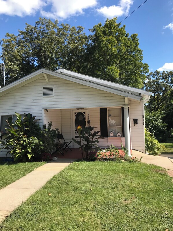 A single-story house with a front porch, a small garden, and a clear blue sky.