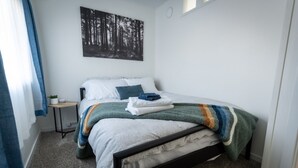 A neatly made bed with a striped blanket, a small bedside table with a plant, and a forest-themed wall art. - PRIVATE Main-Level Suite for Work & Play (Lethbridge)