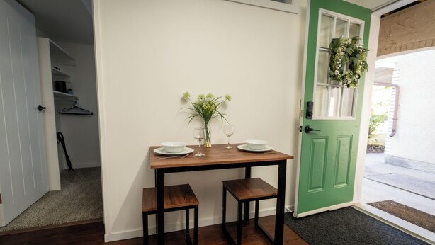 A dining area with a table, two chairs, a vase with flowers, and a green door. - PRIVATE Main-Level Suite for Work & Play (Lethbridge)