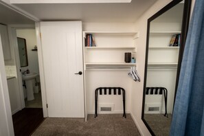 A small, well-lit room with a white door, a mirror, a radiator, and a shelf with books.