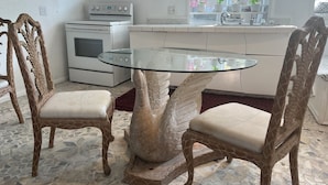 A kitchen with a glass-top table surrounded by two giraffe-themed chairs, a white stove, and a window with potted plants.