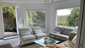 A modern living room with a glass coffee table, two patterned armchairs, a sofa, and a large window offering a view of greenery.