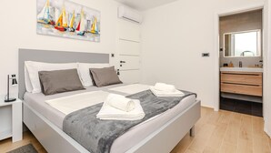Et moderne soveværelse med en stor seng, et natbord, et sminkebord, et maleri, en aircondition og et badeværelse med spejl og vask.