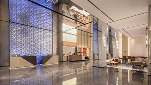A modern hotel lobby with a reflective floor, a reception desk, seating area, and a decorative wall with a geometric pattern. - Microtel BY Wyndham Maoming Dianbai (Maoming)