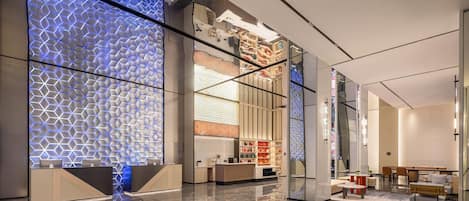 A modern hotel lobby with a reflective floor, a reception desk, seating area, and a decorative wall with a geometric pattern.
