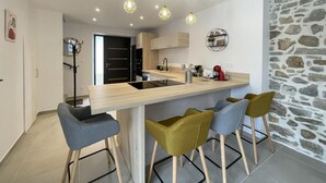 Une cuisine moderne dotée d’un îlot central, de tabourets de bar, de luminaires suspendus et d’un mur d’accent en pierre.