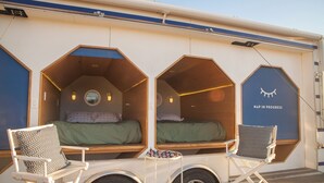 Una cabaña con dos espacios hexagonales para dormir, cada uno con una cama y una almohada, y una pequeña mesa con aperitivos.