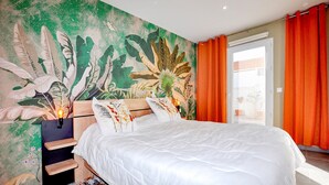 Ein Schlafzimmer mit einem großen Bett, einem Nachttisch, einem Wandbild und orangefarbenen Vorhängen.