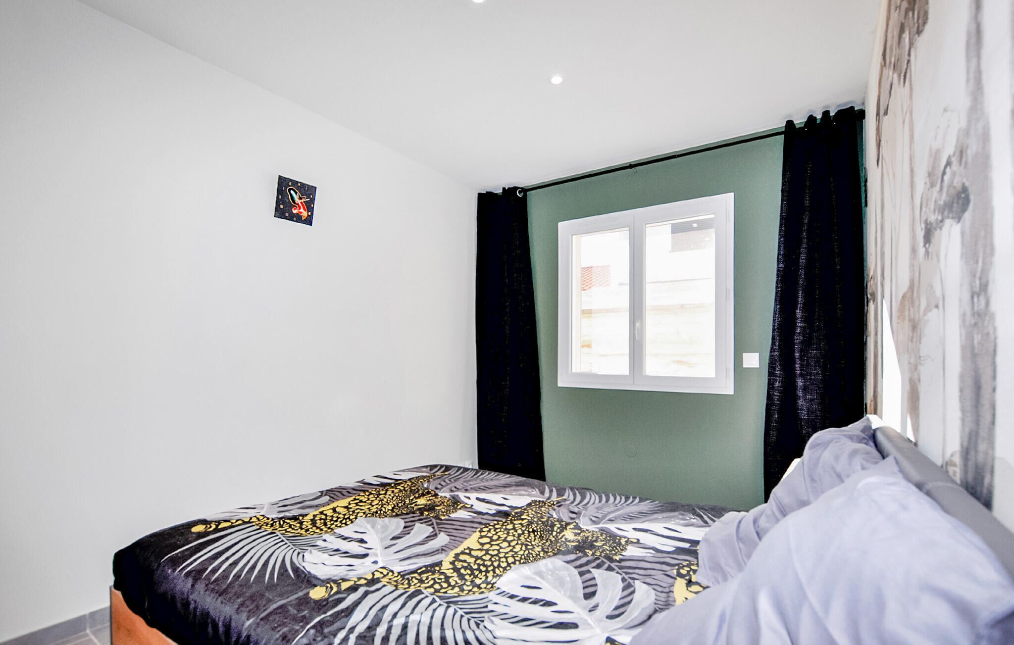 Une chambre à coucher avec un lit, une fenêtre avec des rideaux et un petit tableau accroché au mur.