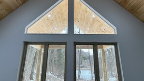 Ein Zimmer mit schräg verlaufender Holzbalkendecke, zwei Oberlichtern und großen Fenstern mit Blick auf eine verschneite Landschaft.