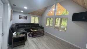 Ein Wohnzimmer mit einem Ecksofa, einem Couchtisch und einem an der Wand montierten Fernseher.