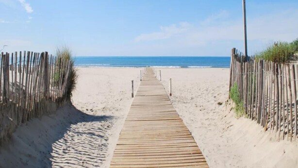 En träpromenad som leder till en strand med sanddyner på vardera sidan.
