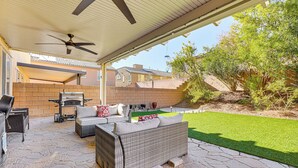 Eine Terrasse im Freien mit Steinböden, einem Deckenventilator, einem Grill und einer Sitzgruppe mit einer Couch und Sesseln.