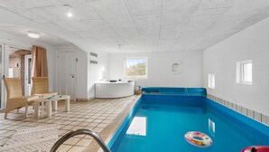 Una piscina interior con suelo de baldosas azules y blancas, un jacuzzi y un ventanal que proporciona luz natural.
