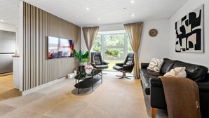 Una sala de estar moderna con televisor de pantalla plana, sofás de cuero, una mesa de centro y un ventanal con cortinas.