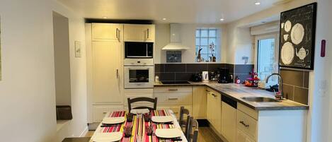 A modern kitchen with white cabinetry, a dining table set for four, and a kitchen island with a sink.
