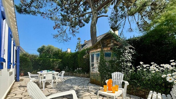 An outdoor patio with white plastic chairs and tables, a small white building, and a white picket fence.
