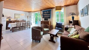 A spacious living area with a wooden ceiling, a dining table with chairs, a sofa, and a television.
