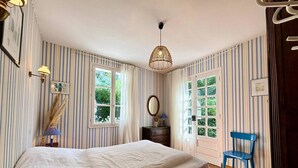 A bedroom with striped wallpaper, a bed, a dresser, a chair, and a hanging light fixture.
