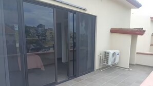 A balcony with a sliding glass door, an air conditioning unit, and a view of buildings in the background. - Suite Hab. 6, Campo de Golf, En Zona de Hotelería, Playa, Barra & Balcón privado (San José del Cabo)