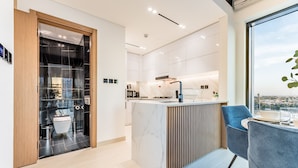 A modern kitchen with white cabinets, a marble island, and a view of the city. - City Views 1BR Close to Golf Course & Attractions, Binghatti Venus, Jumeirah Village Circle (Dubai)