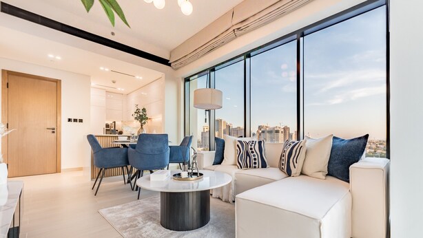 A modern living room with a white sofa, blue chairs, a round coffee table, and a large window offering a city view. - City Views 1BR Close to Golf Course & Attractions, Binghatti Venus, Jumeirah Village Circle (Dubai)